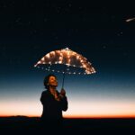 A joyful woman with a light-up umbrella stands under a starry sky, capturing a magical moment.
